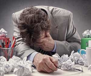 Burned out employee with head on desk surrounded by crumpled paper