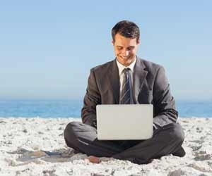 Happy man in suit working on laptop on the beach