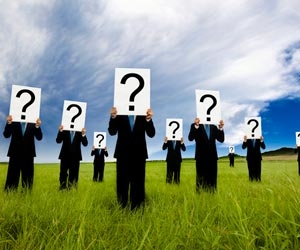 Businessmen standing in field with questions marks over face