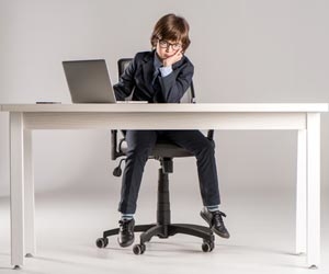 Child in suit sitting at desk but feet don't touch the ground