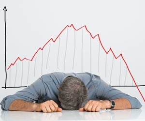 Frustrated man with head on desk sitting in front of a downward trending graph