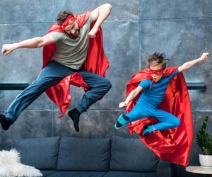 Adult and child in superhero costumes jumping off couch