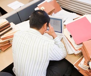 Worker stares at laptop in cubicle and is surrounded by files of work