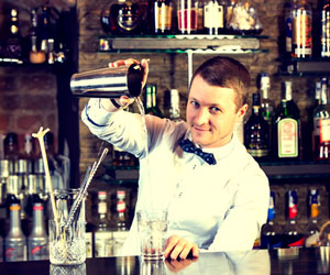 Happy bartender standing behind the bar mixing a fancy cocktail