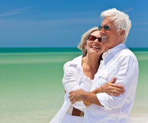 A retired couple smiles while walking along a tropical beach