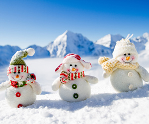 Three snowmen in the snow with blue sky and snowy mountains in the background