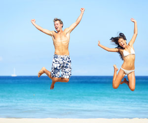 Man and woman in swimsuits jumping into air in front of beach
