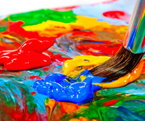 Artist dipping a paintbrush into bright colors on an artist's palette