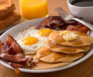 Delicious breakfast of pancakes, eggs, and bacon with orange juice and coffee