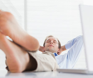 Man at work with laptop open and bare feet propped up on desk while taking a nap