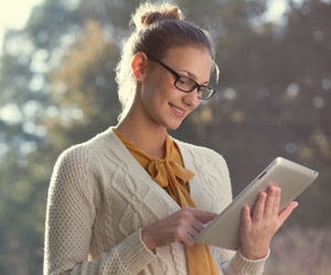 Woman standing outside and smiling while using a tablet