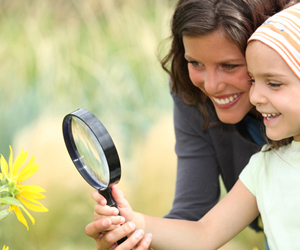 Babysitter and child looking at yellow flower with magnifying glass