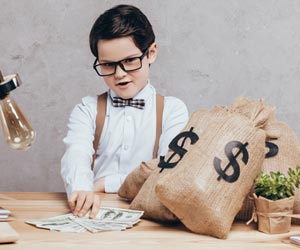 Boy dressed in bowtie surrounded by money bags and counting cash